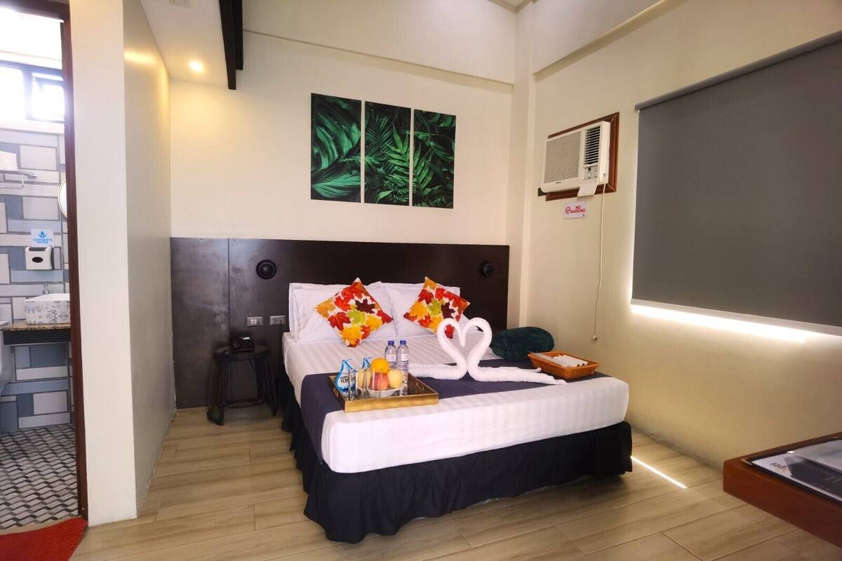 A hotel room with a bed, a nightstand, a wall-mounted air conditioner, and a window.