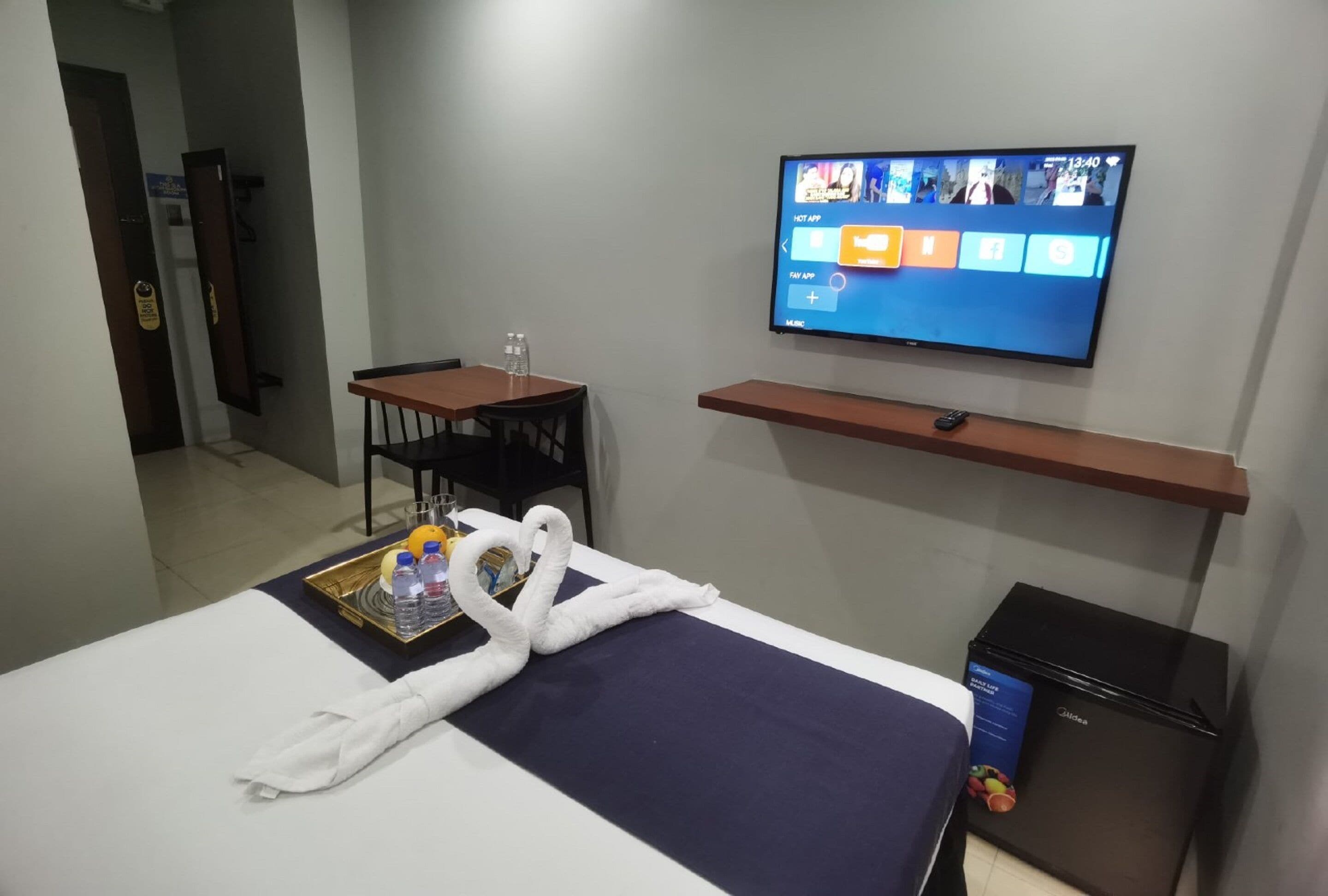 A hotel room with a bed, a TV mounted on the wall, a desk, and a small refrigerator.
