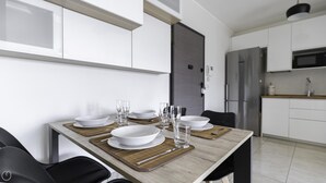 A modern kitchen with white cabinets, a stainless steel refrigerator, and a dining area with a wooden table set for four. - Tognazzi 6 in Milan With 1 Bedrooms and 1 Bathrooms (Milan)