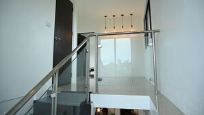 Eine moderne Treppe mit Glasgeländern und einem Metallhandlauf, die zu einer Zwischenebene mit Blick ins Freie führt.