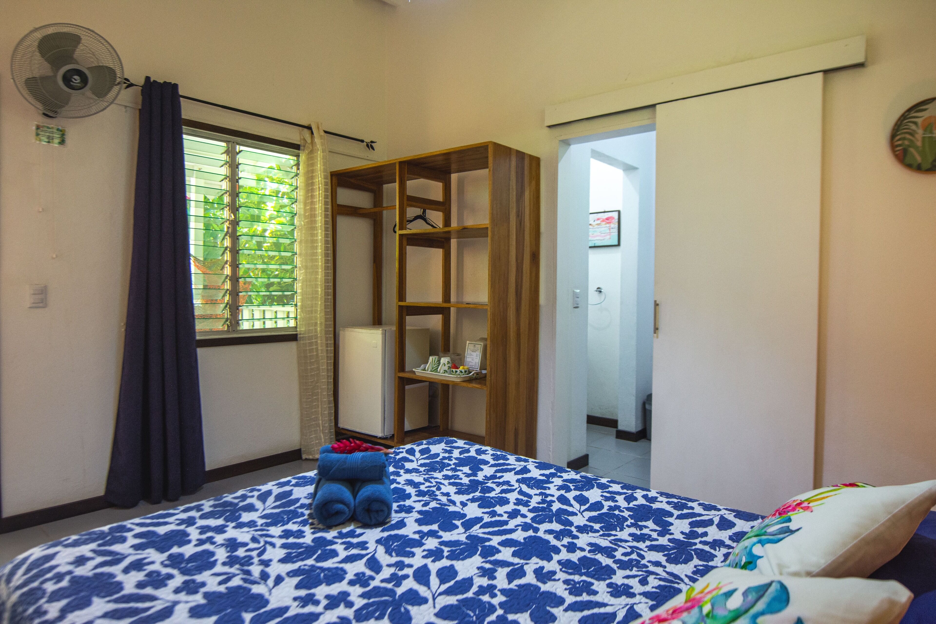 A bedroom with a bed, a wardrobe, a fan, and a window with curtains.