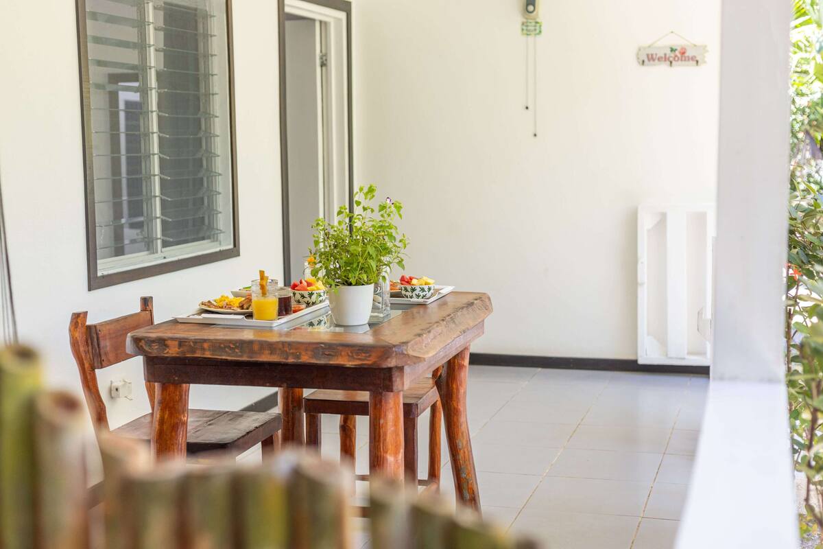 A wooden dining table with chairs, a potted plant, and a breakfast setting with plates and a pitcher of orange juice.