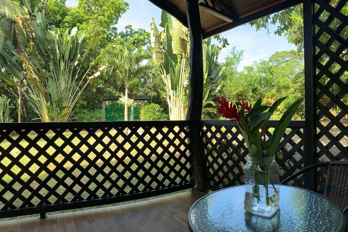 A glass table with a vase of flowers on a balcony with a lattice fence.