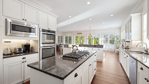 A spacious kitchen with white cabinetry, a granite countertop, stainless steel appliances, and a view of the outdoors.