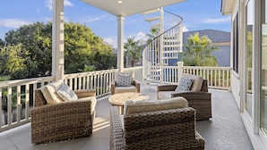A covered outdoor area with wicker furniture, a spiral staircase, and a view of a building in the background.