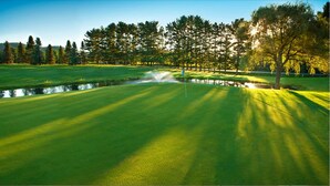 Un parcours de golf avec des obstacles d’eau, des arbres et un ciel dégagé.