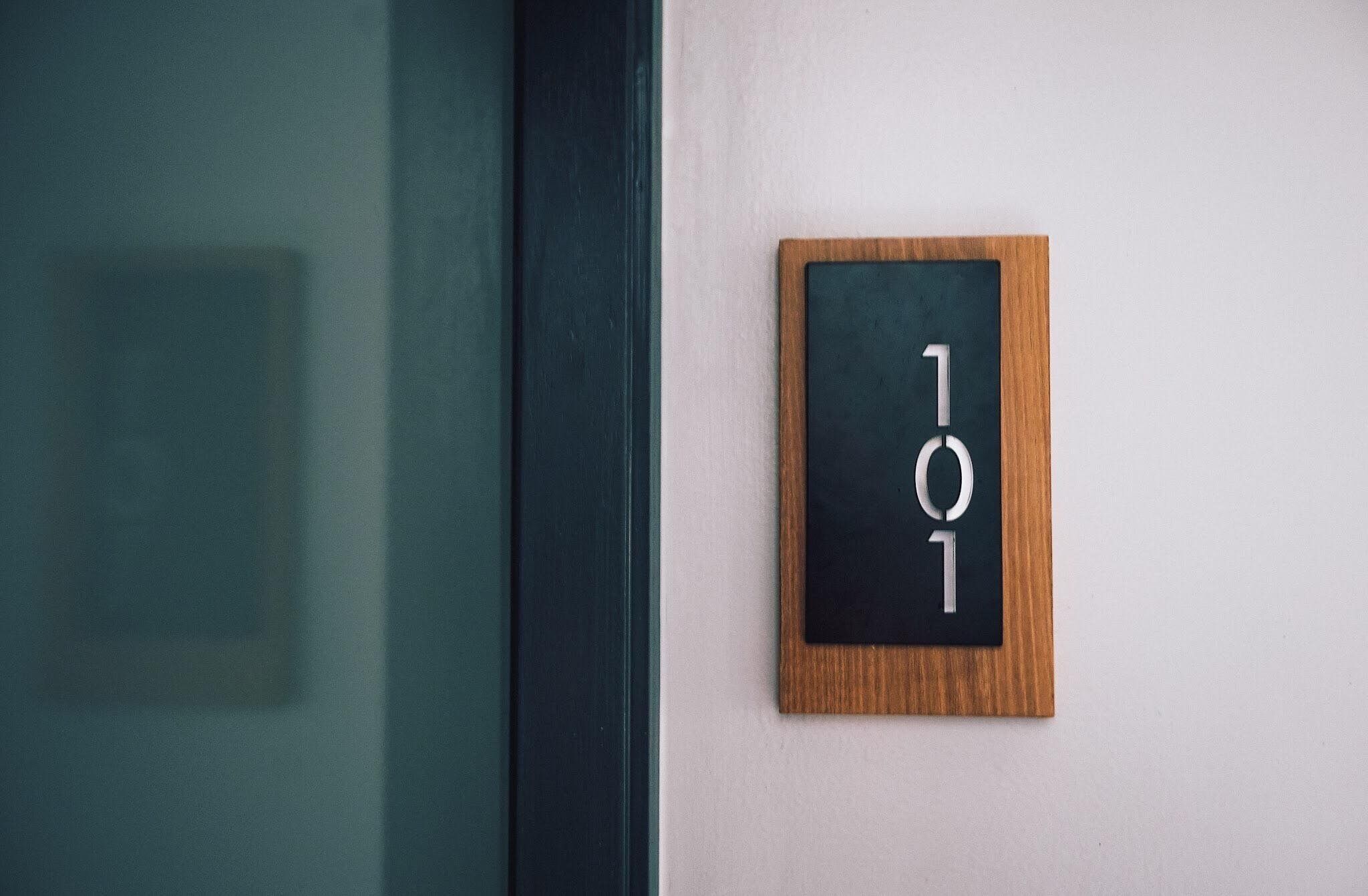 A wooden-framed sign with the number "101" on a white wall.