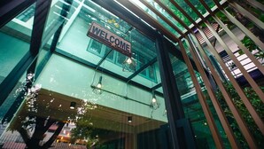 A modern building with a 'WELCOME' sign, large windows, and hanging light fixtures. - Bed Garden 26 (Bangkok)