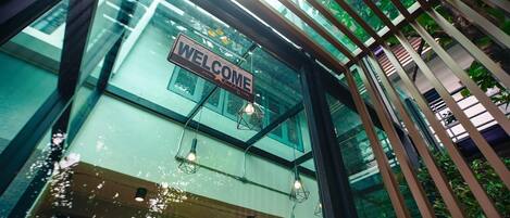 A modern building with a 'WELCOME' sign, large windows, and hanging light fixtures.