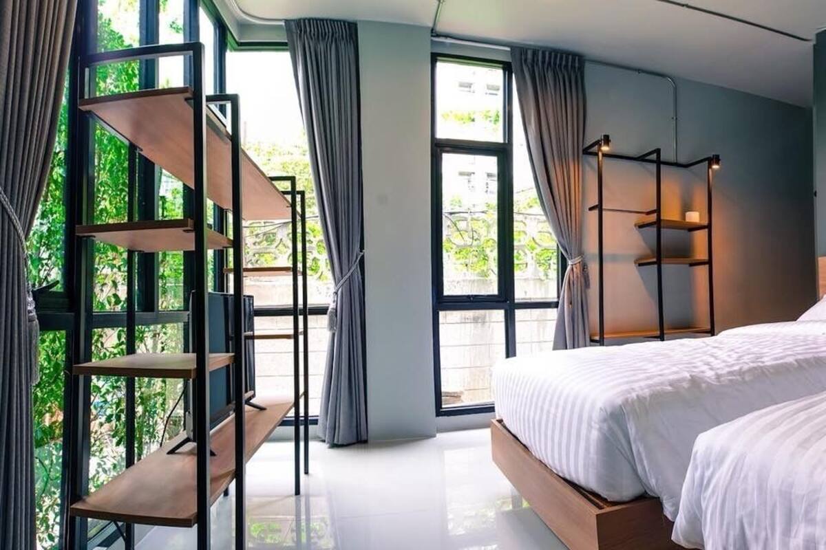 A modern bedroom with two beds, a built-in bench, and a large window with curtains.