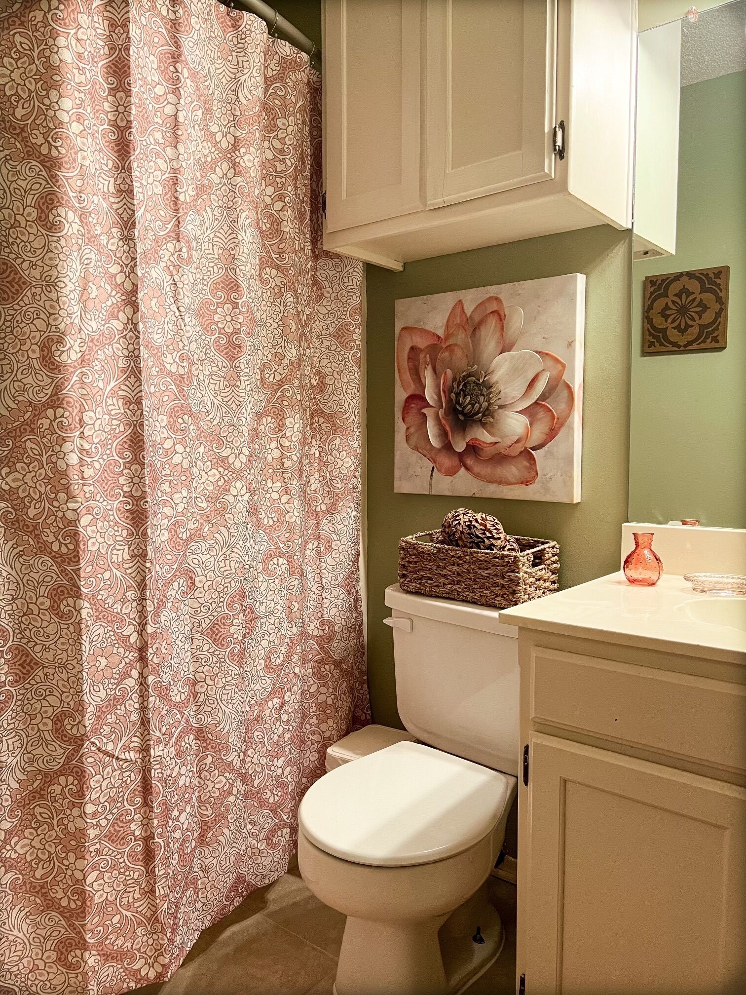 Un baño con inodoro, cortina de ducha, lavabo instalado en la pared y una pintura decorativa de una flor.