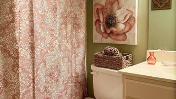Un baño con inodoro, cortina de ducha, lavabo instalado en la pared y una pintura decorativa de una flor.