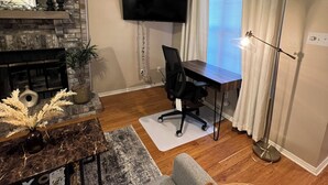 Un salon avec une cheminée, un téléviseur fixé au mur, un bureau et un canapé.