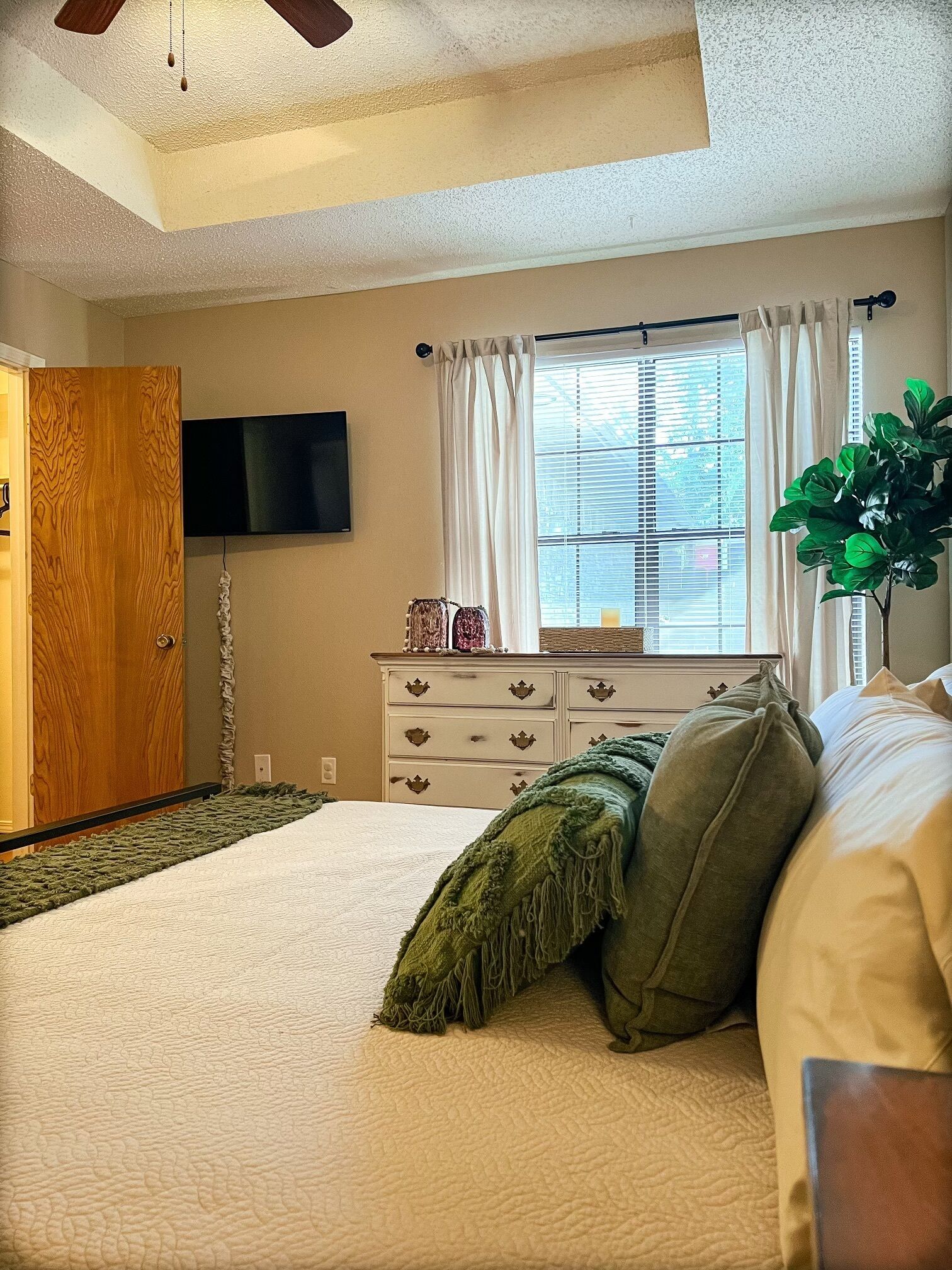 Un dormitorio con una cama, un aparador, un televisor y una ventana con cortinas.