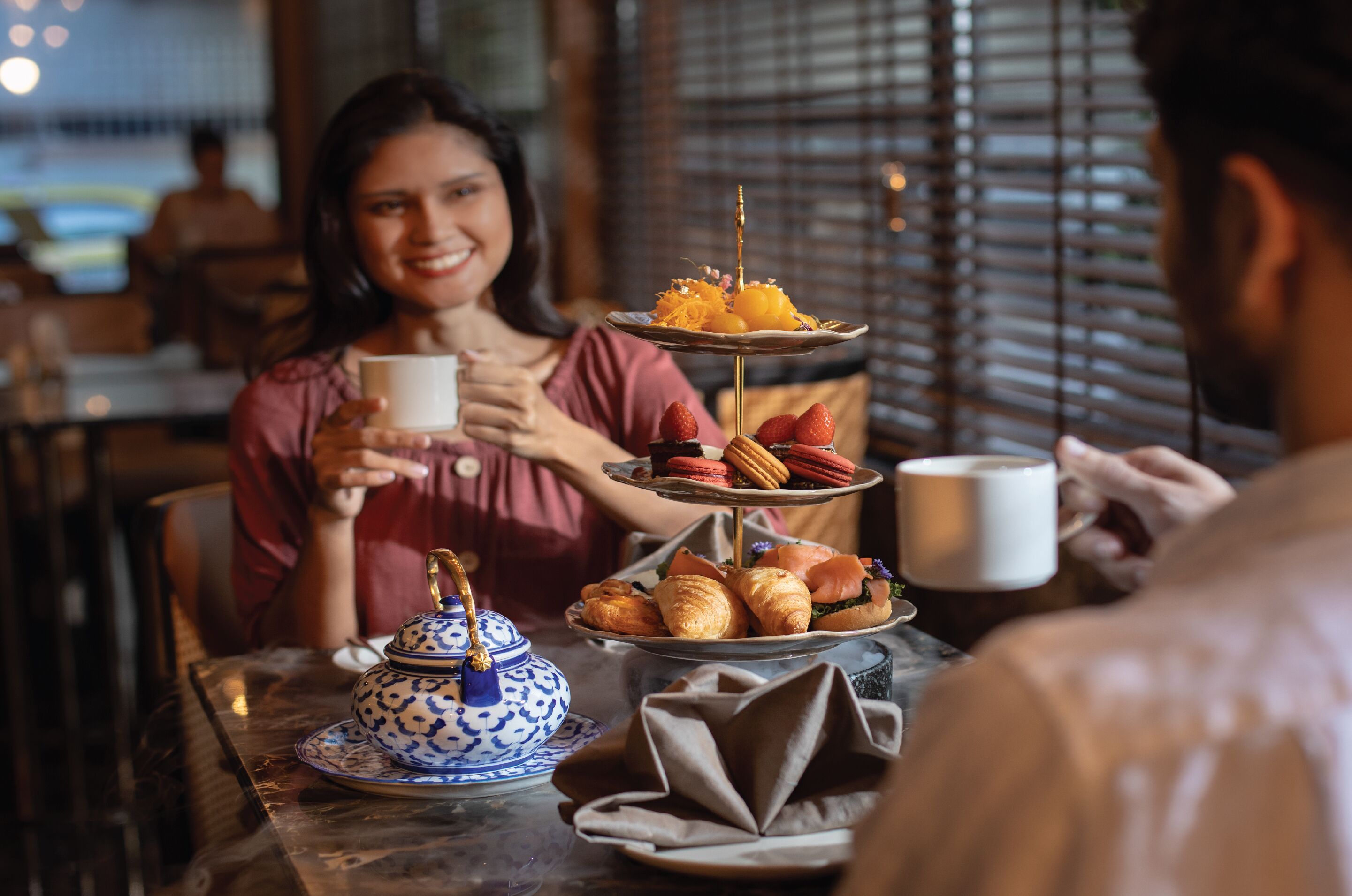 A dining table with a teapot, a tiered dessert stand, and a cup.