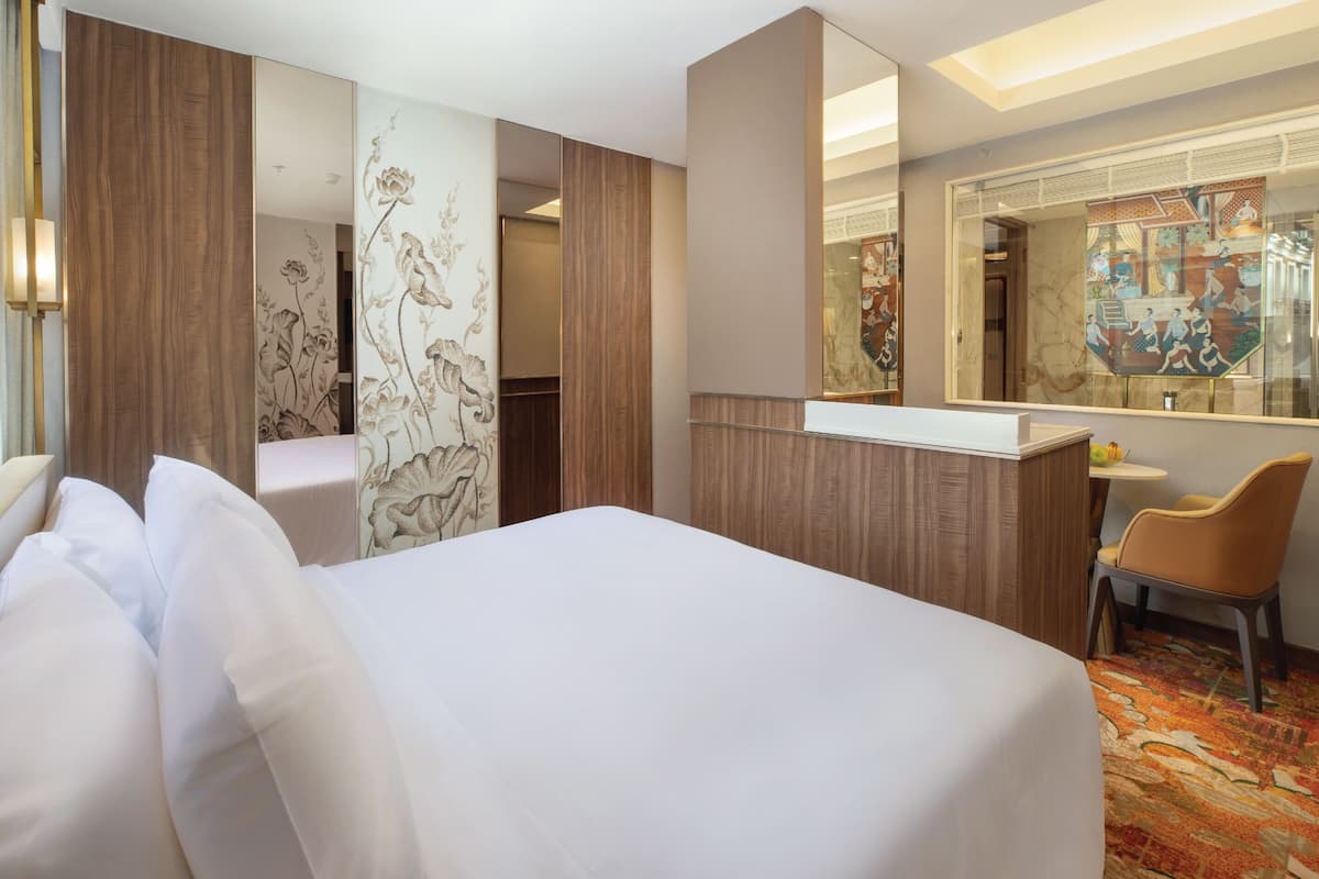 A hotel room with a large bed, a desk with a chair, a mirror, and a decorative wall panel.