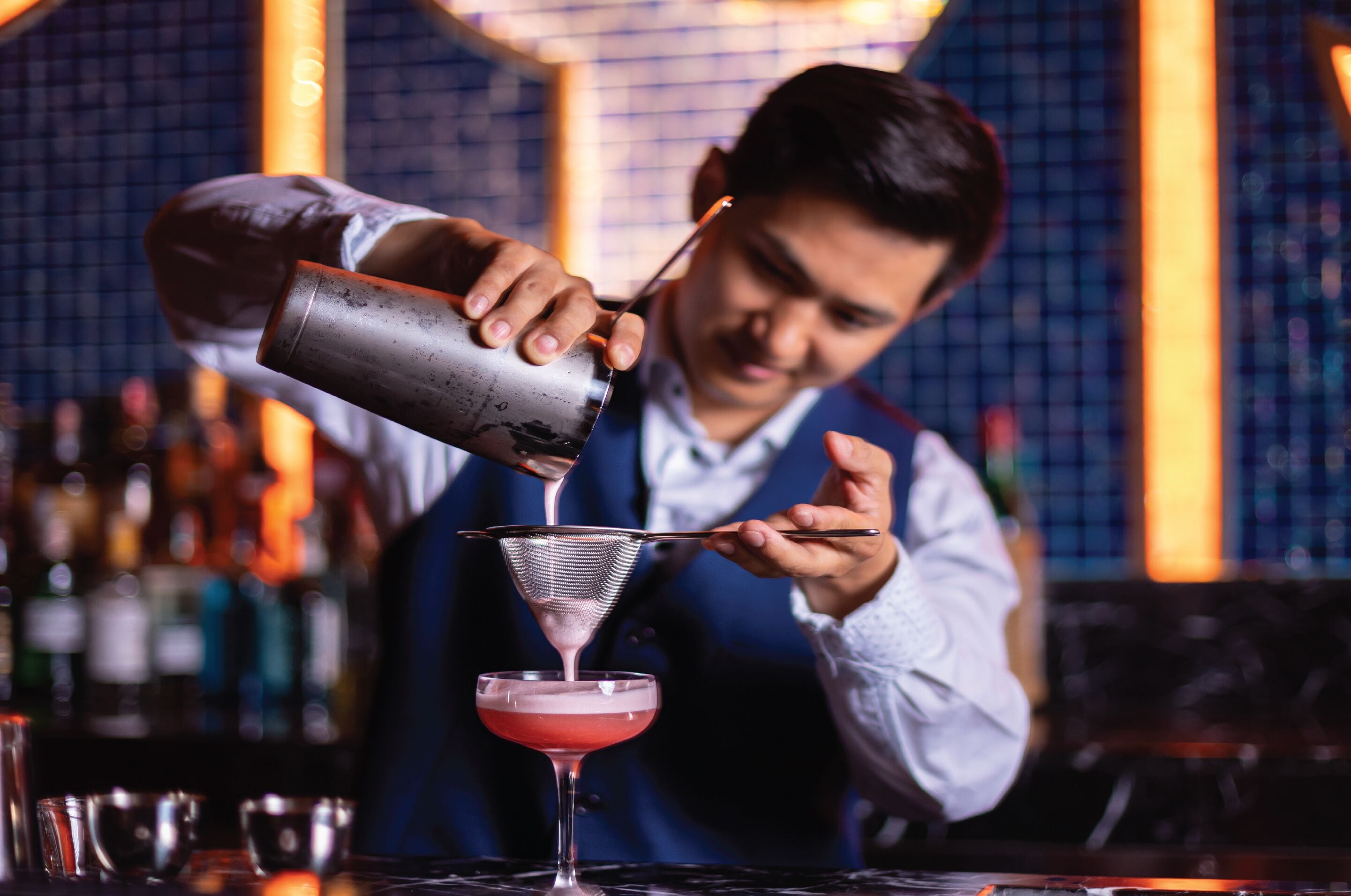 A bartender pouring a drink into a martini glass.