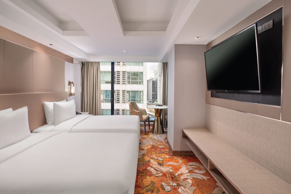 A hotel room with two beds, a TV, a small table with a chair, and a view of the city.