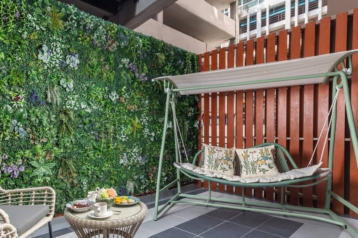 A patio with a swing chair, wicker furniture, and a green wall with plants.