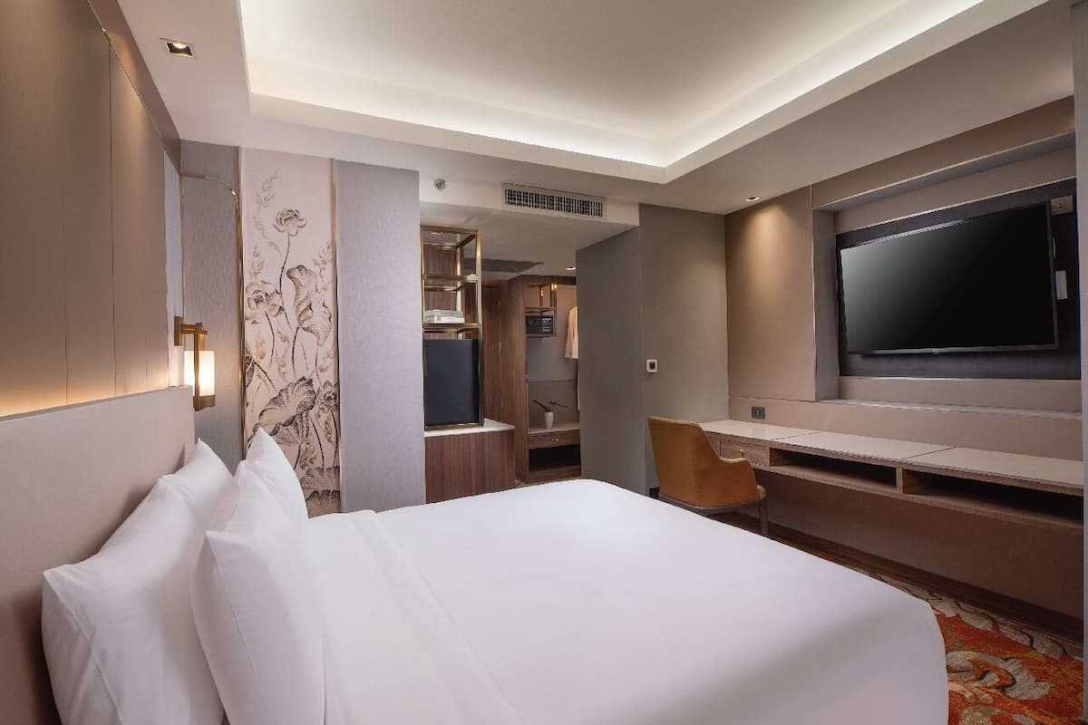 A hotel room with a large bed, a TV, a desk, and a chair.