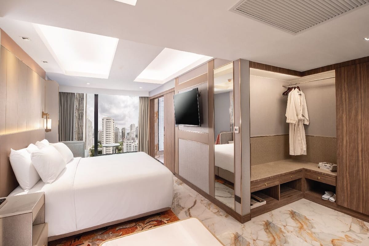 A modern hotel room with a large bed, a TV, a walk-in closet, and a city view.