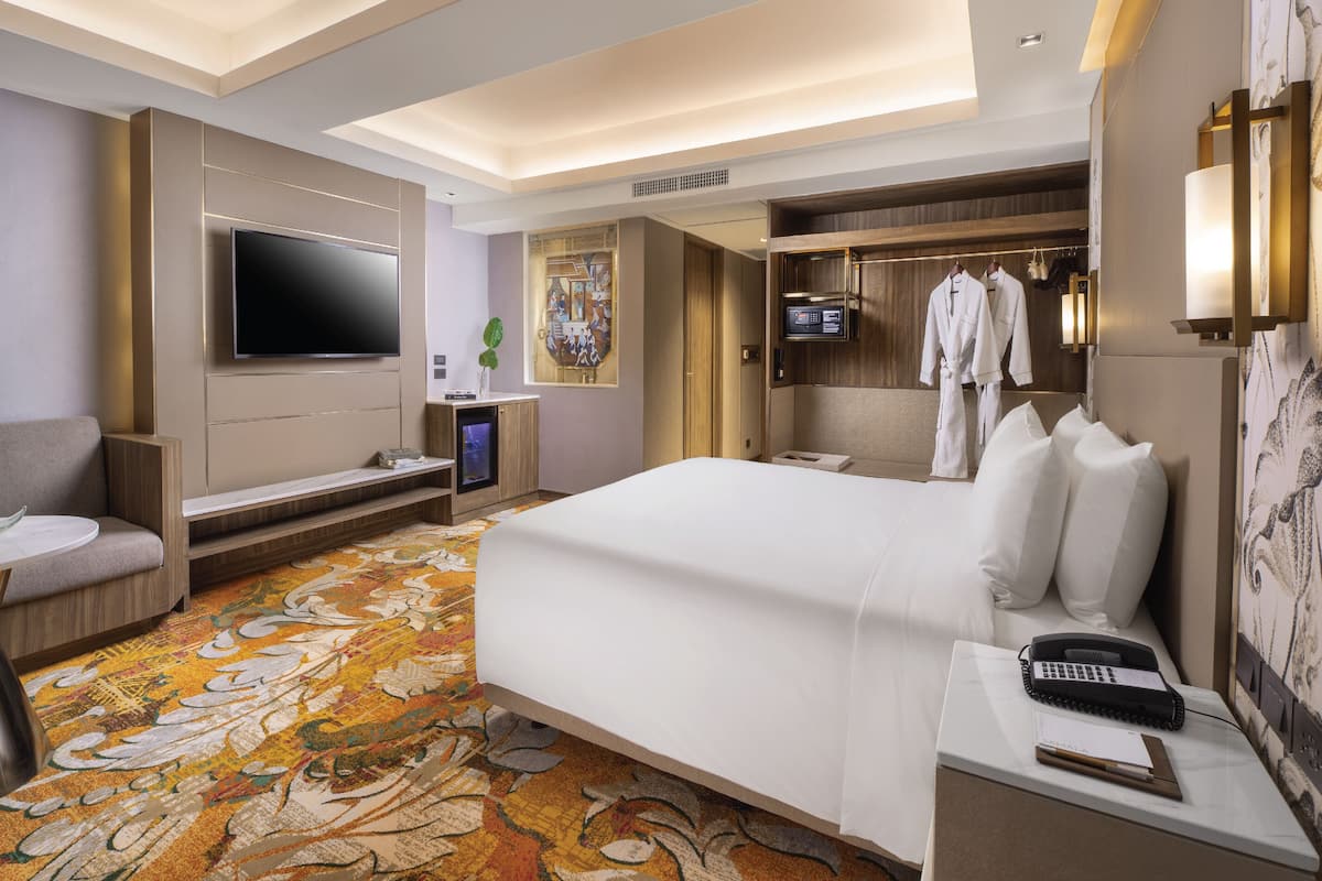 A hotel room with a large bed, a flat-screen TV, a desk with a telephone, and a seating area with a sofa.