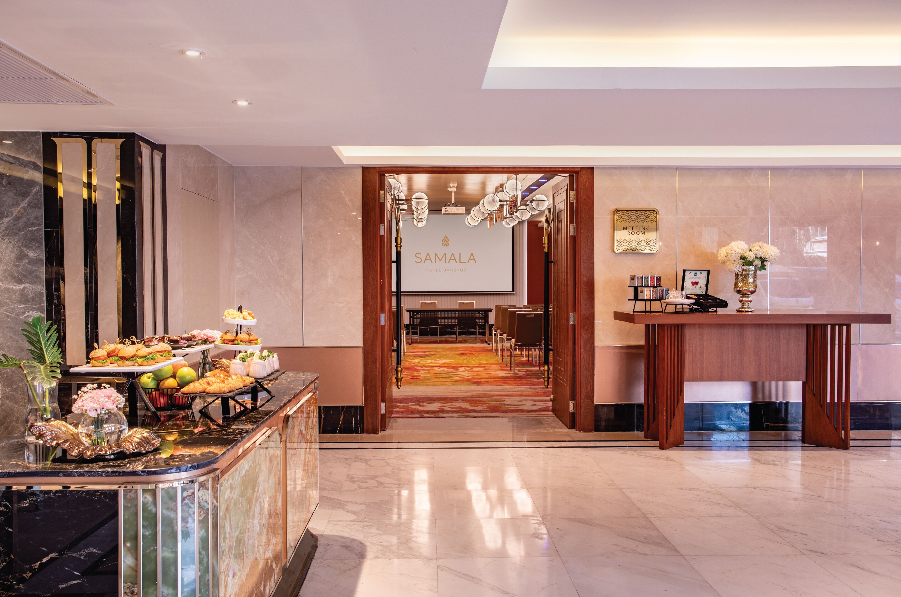 Um saguão de hotel com uma mesa de recepção, espaço para buffet e uma sala de conferências.