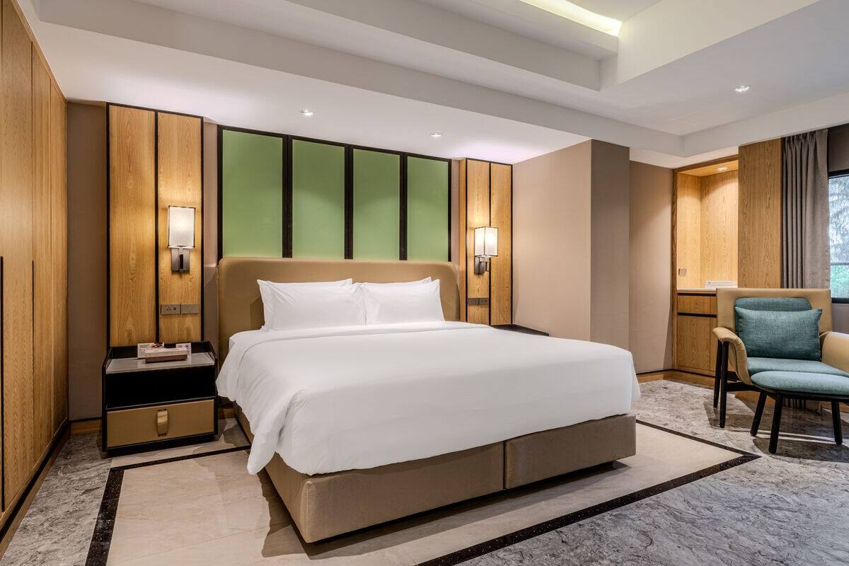 A hotel room with a large bed, wooden panel walls, a nightstand, a chair, and a window.