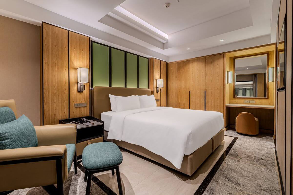 A modern hotel room with a large bed, a desk, a chair, and a mirror.