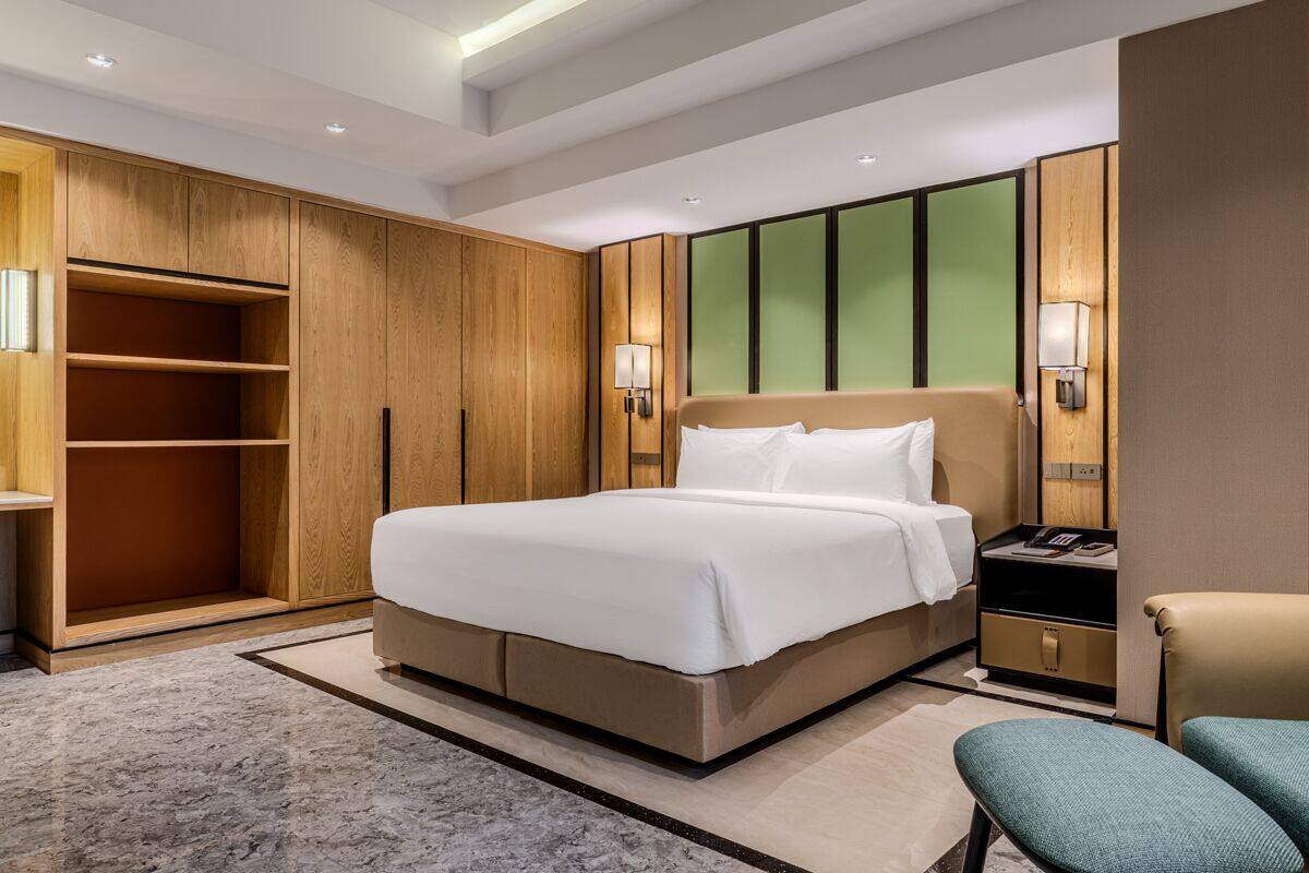 A hotel room with a large bed, wooden wardrobe, bedside tables, and a seating area.
