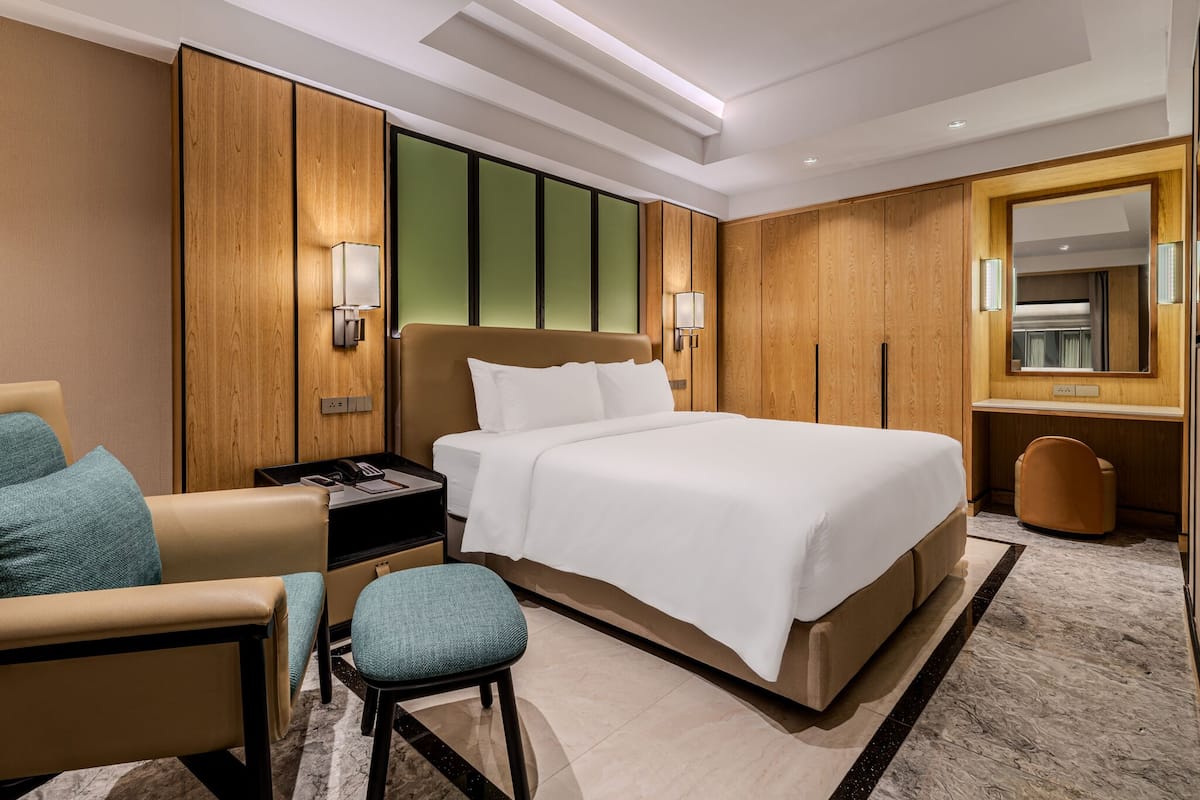 A modern hotel room with a large bed, a desk, a chair, and a mirror.