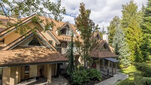 A multi-story house with a covered porch, a landscaped garden, and a variety of trees. - Ski in, Free Shuttle, Walk to Village (Whistler)