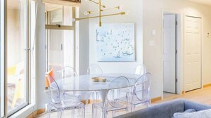 A modern dining area with a glass table and chairs, a chandelier, and a painting on the wall. - Ski in, Free Shuttle, Walk to Village (Whistler)