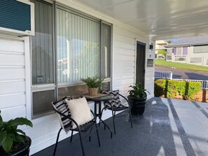 Une véranda abritée avec une table et des chaises, des plantes en pot et une vue sur la rue.
