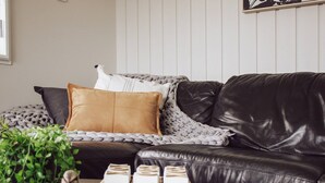 En moderne stue med en sort lædersofa, et gråt strikket tæppe og en brun pude. Et lille bord med en plante og en pynteting står foran sofaen.