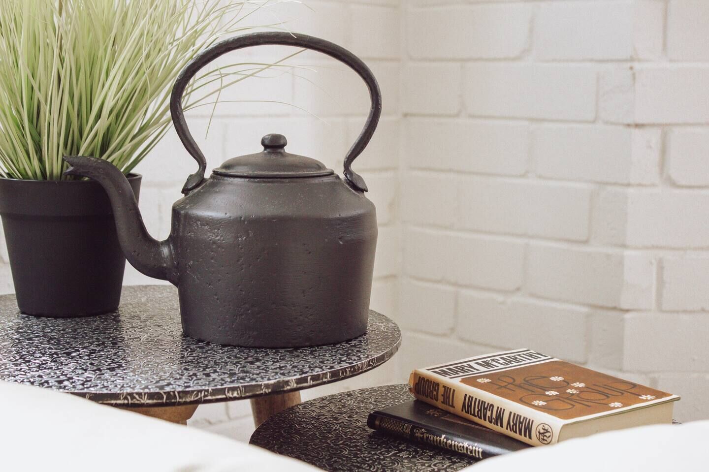 A black teapot on a textured table with a potted plant and two books.