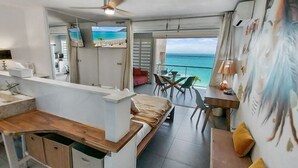 Habitació d'hotel moderna amb zona de cuina, menjador i un balcó amb vista al mar.