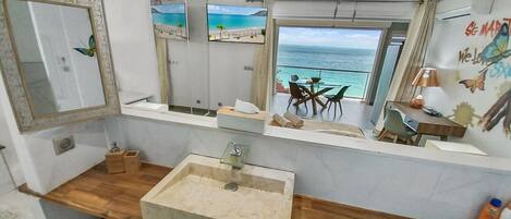 A bathroom with a large mirror, a sink, and a view of the ocean through an open door.