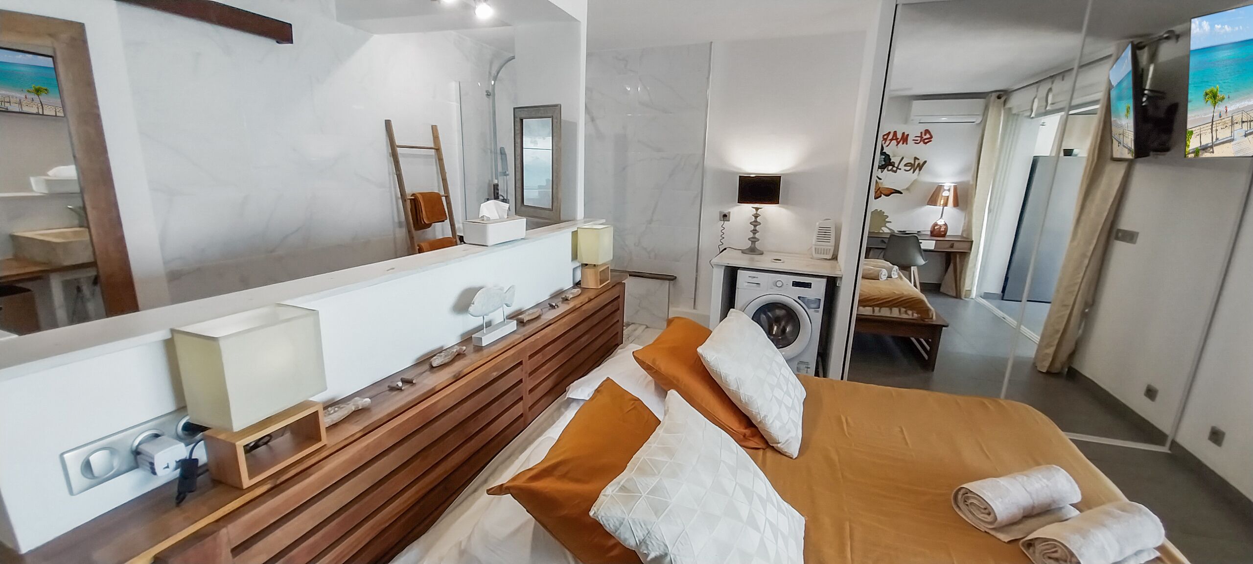 A modern hotel room with a large bed, a wooden dresser, a washing machine, and a large mirror.