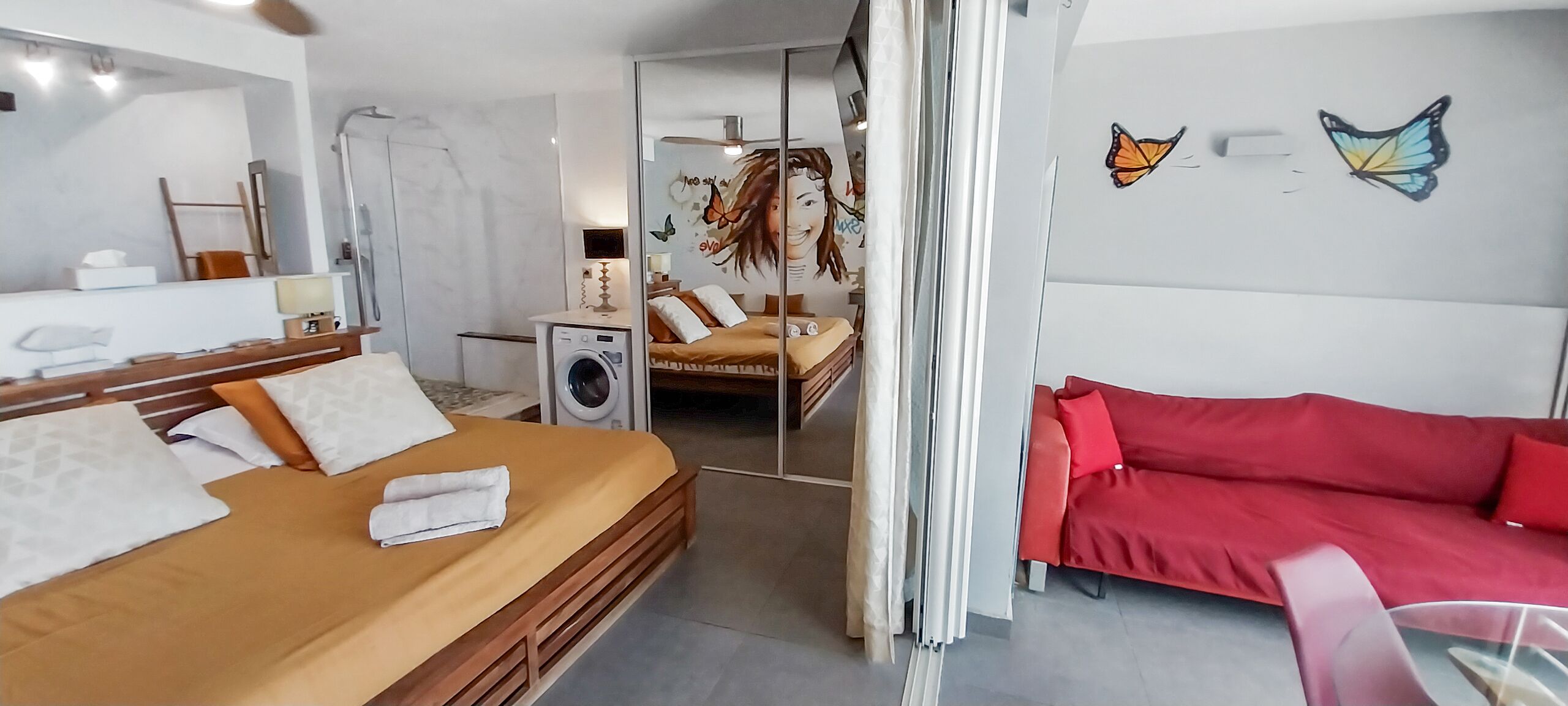 A modern hotel room with a wooden bed, a red sofa, a washing machine, and butterfly wall art.