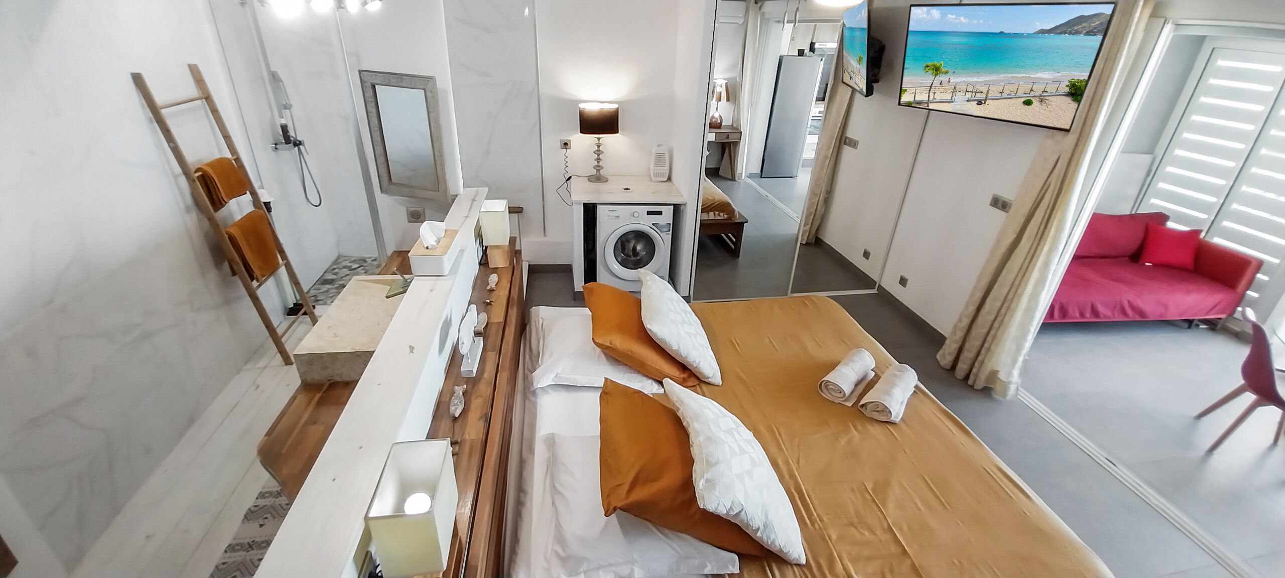 A hotel room with a bed, a washing machine, a desk, a mirror, and a TV.