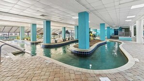 An indoor swimming pool with clear water, surrounded by tiled walkways and blue pillars. - Ocean Front King Suite Landmark Heated pools (Myrtle Beach)