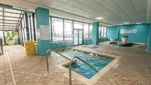 An indoor swimming pool with a tiled floor, a metal pool ladder, and a view of the outside through large windows. - Ocean Front King Suite Landmark Heated pools (Myrtle Beach)