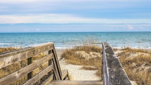 Une promenade en bois menant à une plage de sable où la végétation est clairsemée.