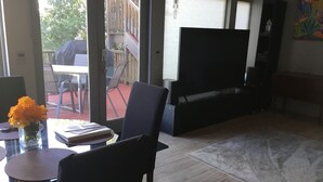 Ein Wohnzimmer mit Flachbildfernseher, einem Esstisch mit Stühlen, einem Couchtisch und einer Vase mit Blumen.