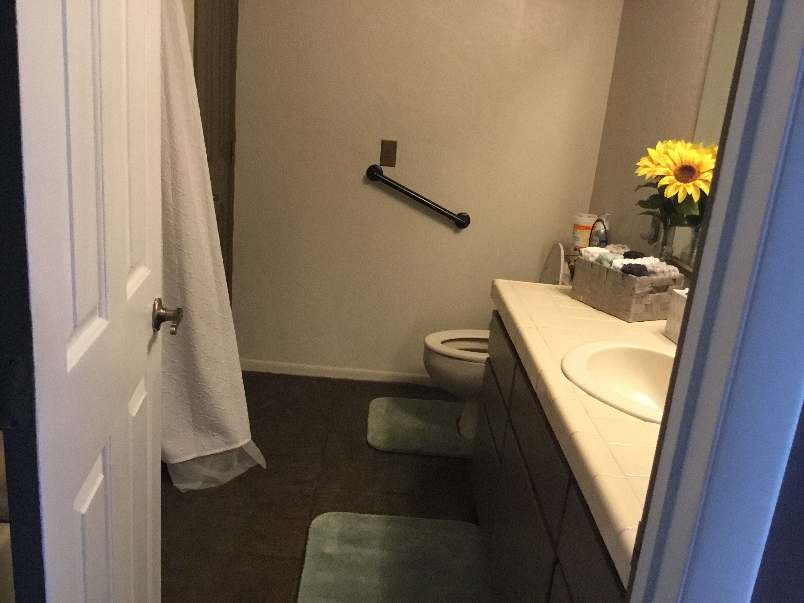 Een badkamer met een wit toilet, een wastafel en een spiegel. Er hangt een handdoek aan de deur.