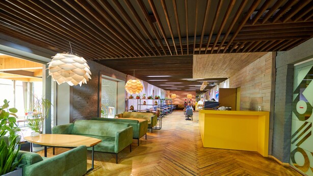 A modern interior with wooden floors, green seating, and a yellow reception desk. - City Hostel (Shymkent)