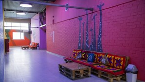 A colorful interior with a long bench, a trash bin, and a wall with a giraffe mural. - City Hostel (Shymkent)