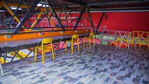 A spacious room with a long table and yellow chairs, a red wall, and a patterned floor. - City Hostel (Shymkent)