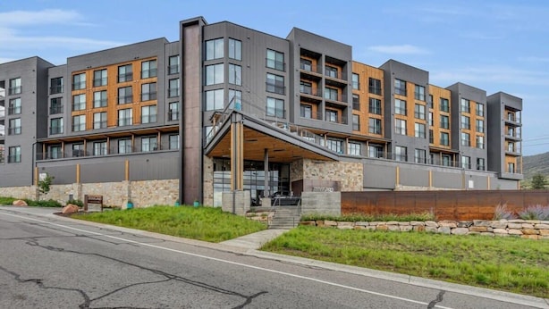 Un immeuble à plusieurs étages doté d’une architecture moderne, caractérisé par un mélange de matériaux en bois et en métal, et une entrée imposante avec une rampe d’accès.